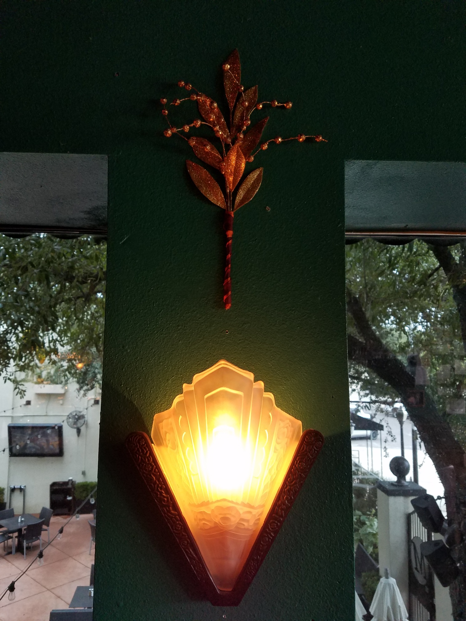 Warm wall light fixture with decorative art above, framed by windows showing outdoor greenery.