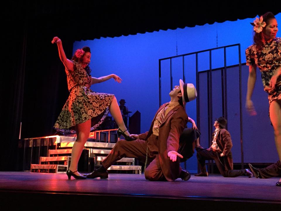 A lively theatrical dance scene with actors in vintage costumes on stage.
