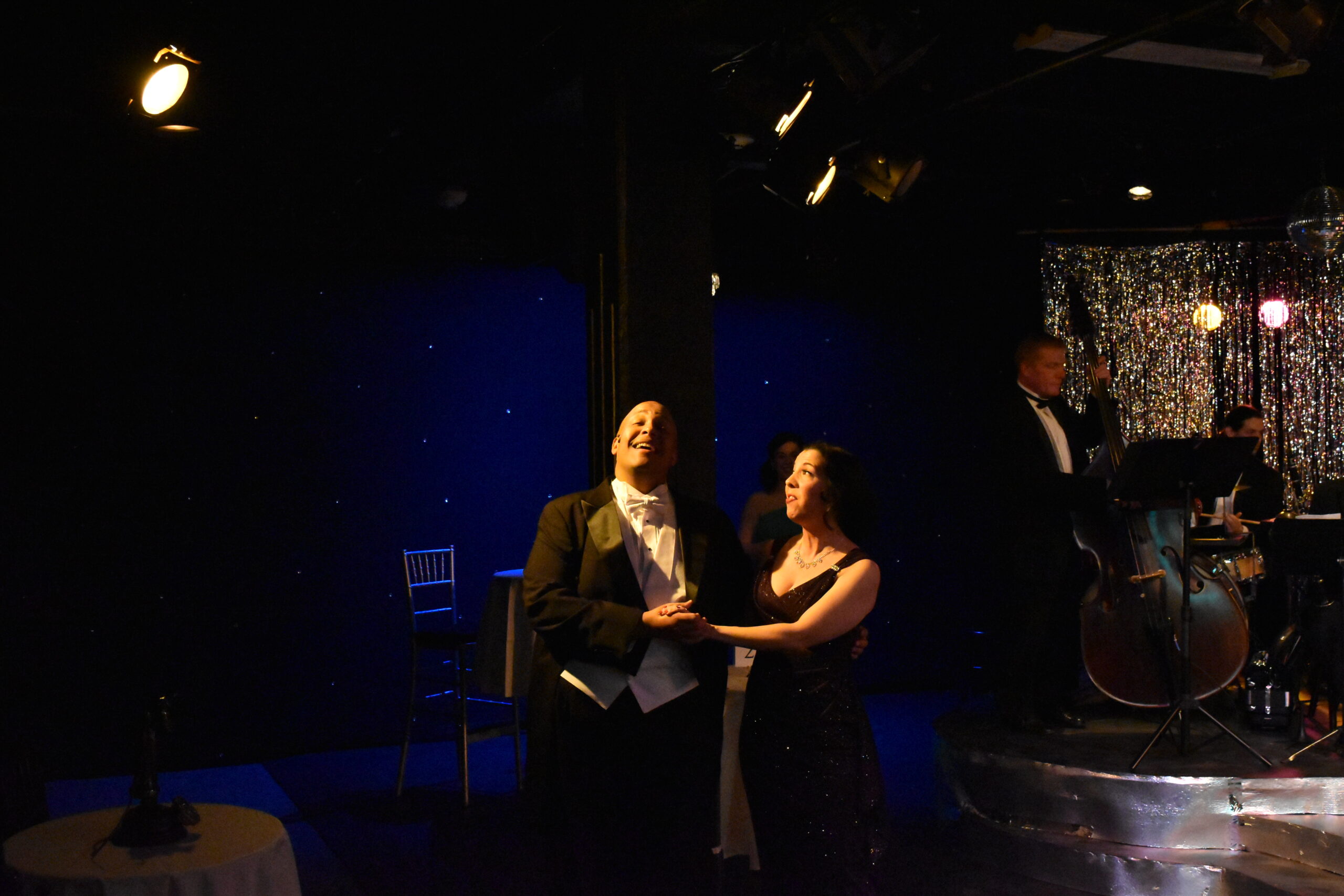 Two people perform a dramatic scene on a dimly lit stage.