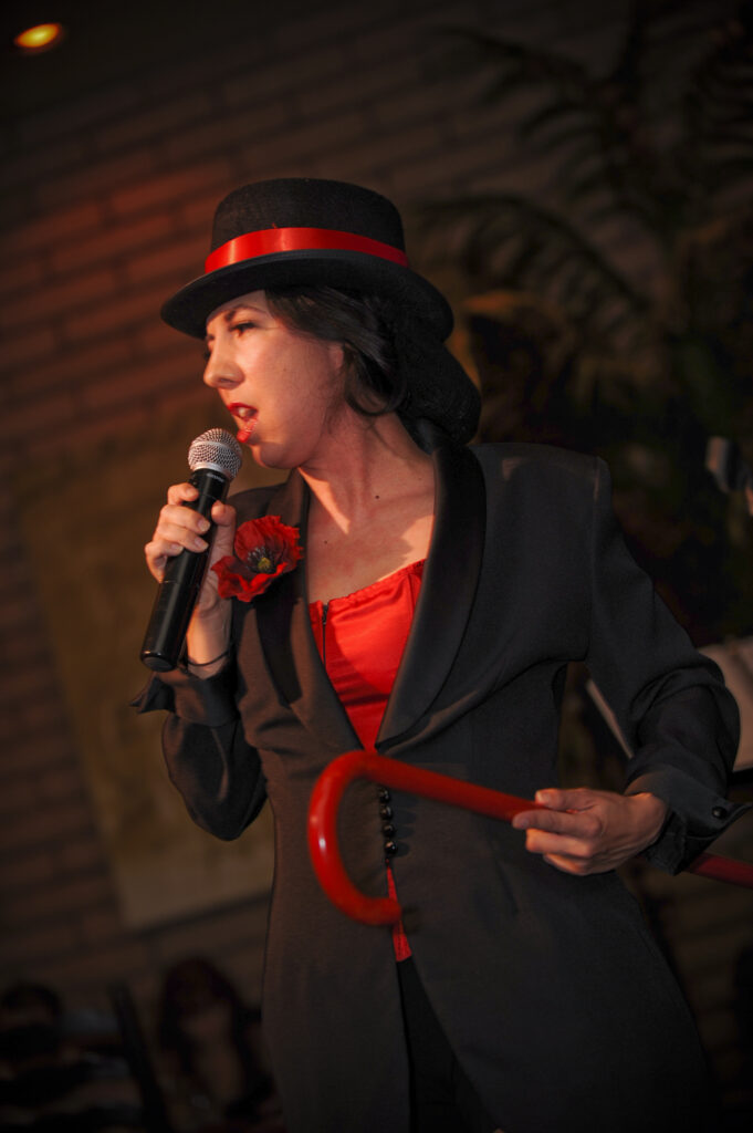 A performer passionately singing into a microphone wearing a black hat and red outfit.