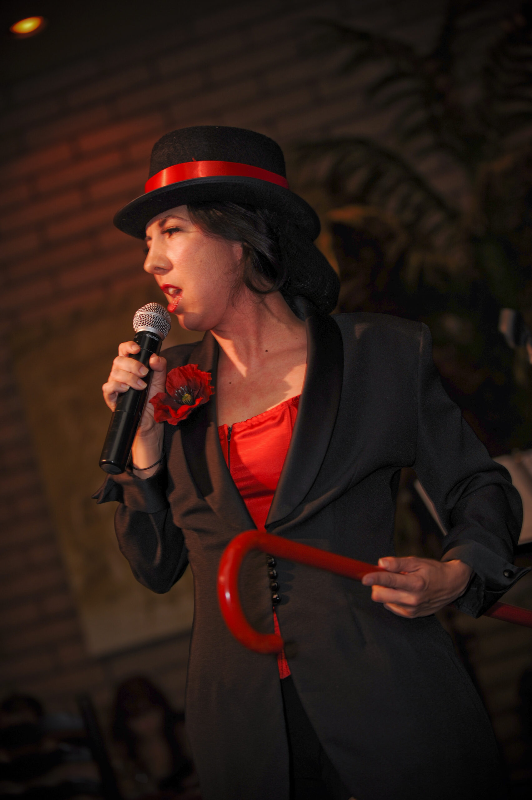 A performer passionately singing into a microphone wearing a black hat and red outfit.