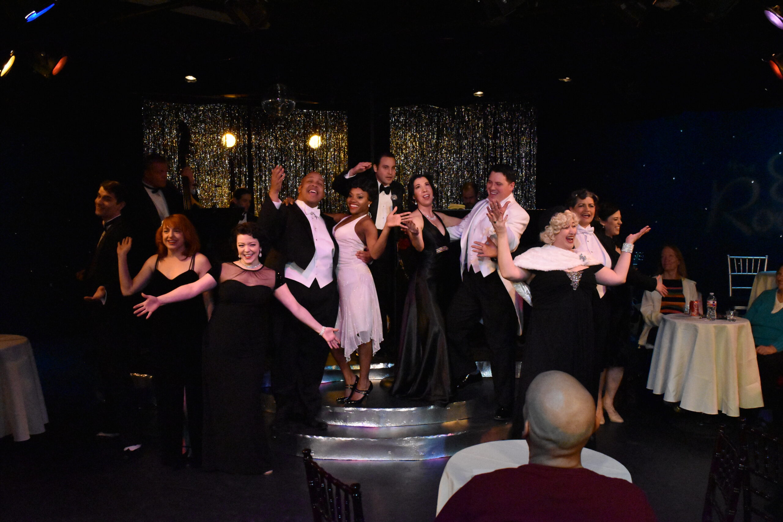 Performers in formal attire on stage during a theatrical scene.