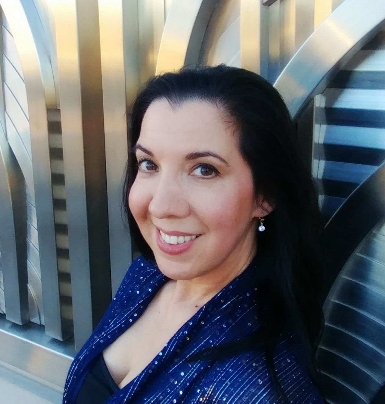 A woman smiling in a blue sequined dress against a metallic background.