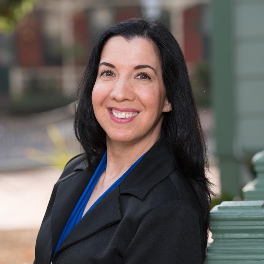 Professional woman smiling outdoors in business attire.