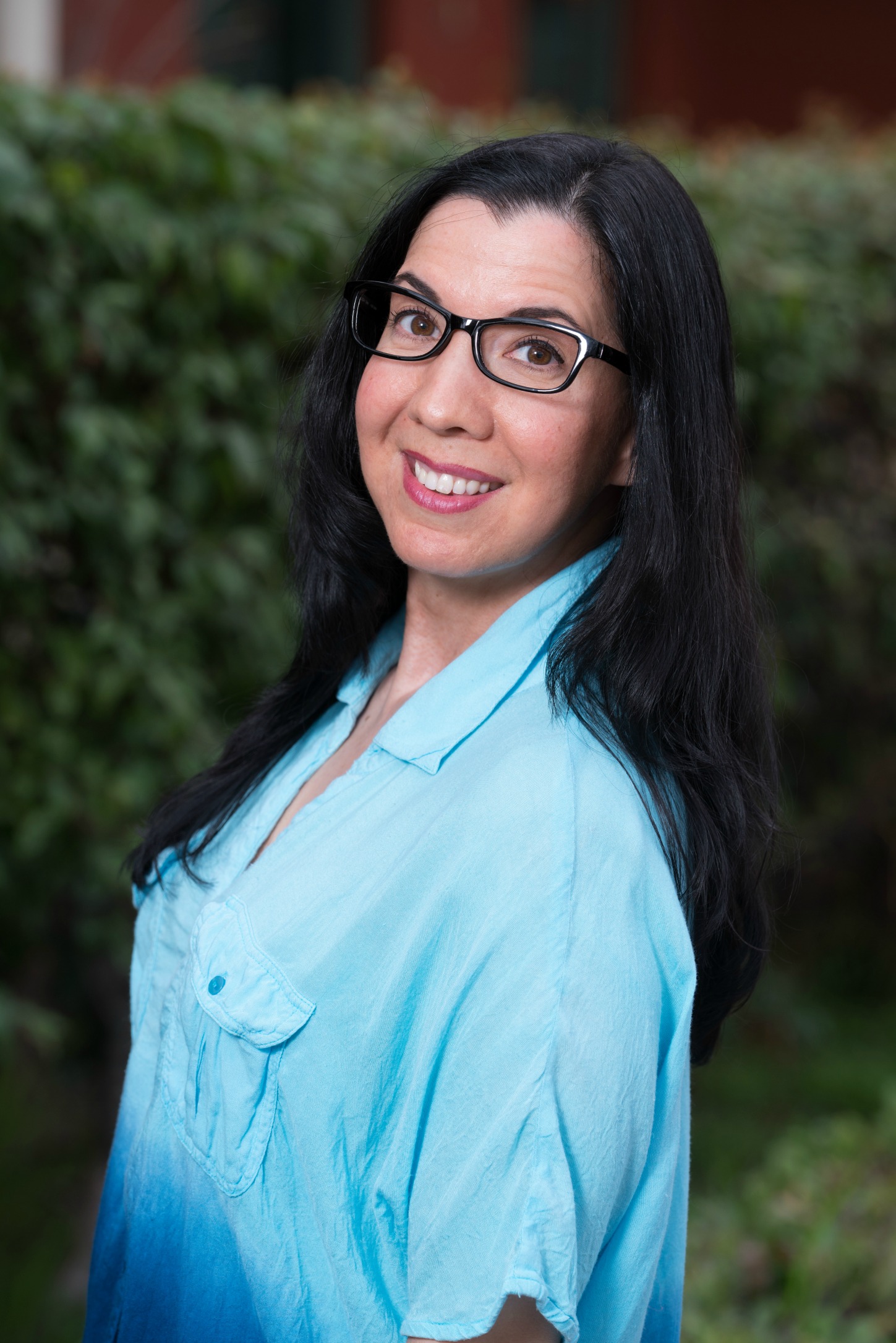 Smiling woman with glasses wearing a light blue shirt outdoors.