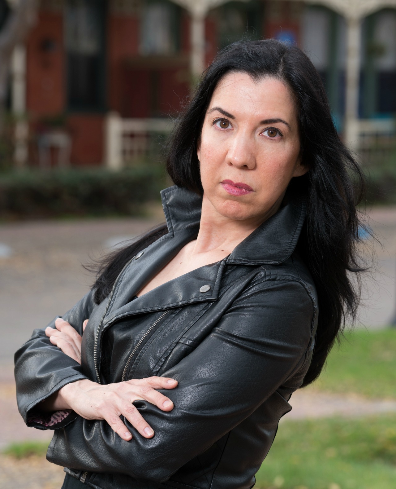 Confident woman in black leather jacket outdoors with arms crossed.