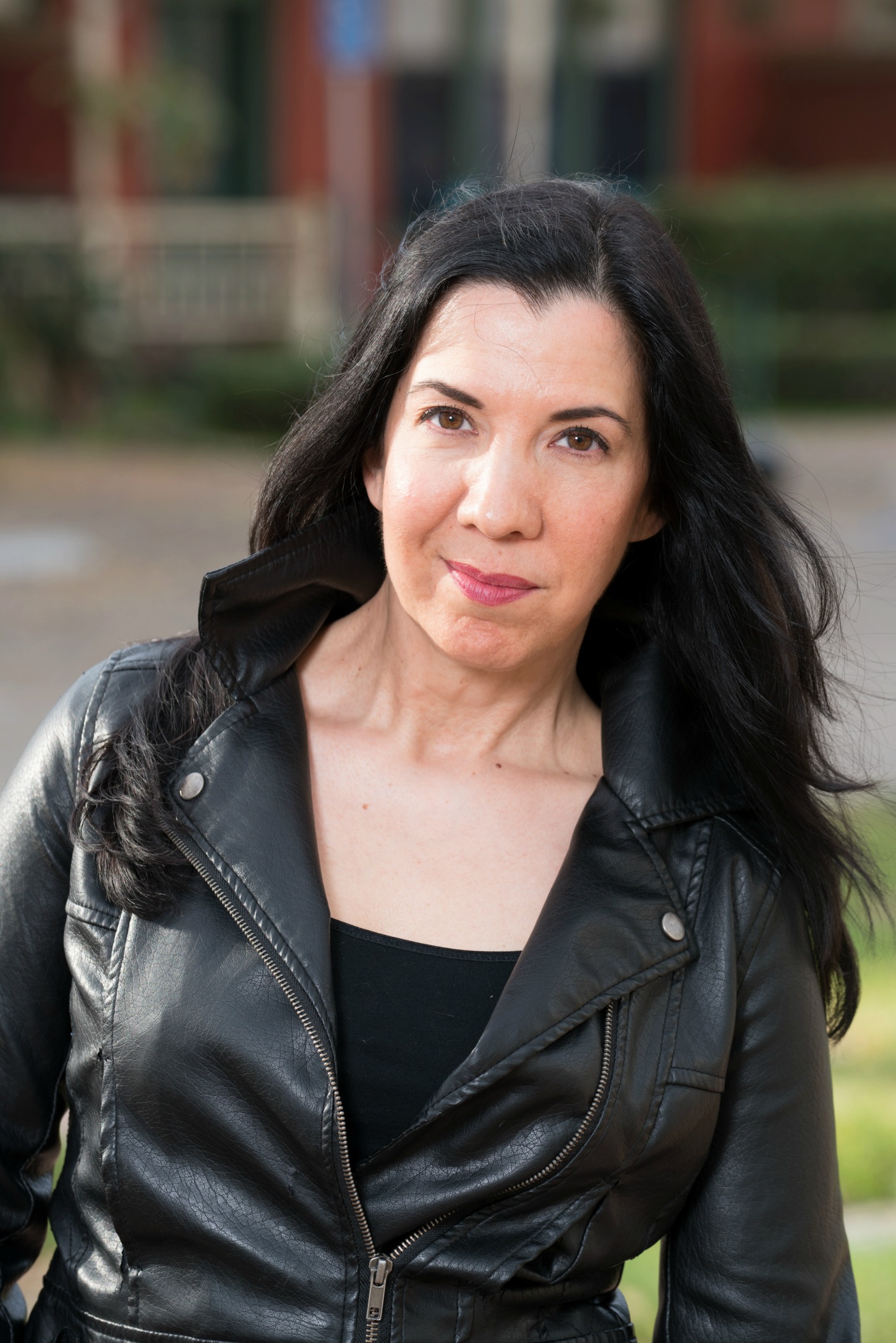 Woman with long dark hair wearing a black leather jacket outdoors.