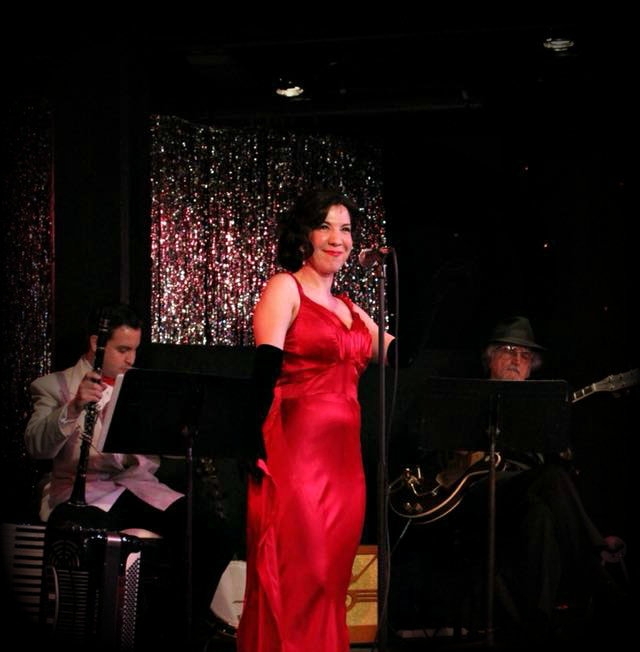 A woman in a red dress sings on stage with musicians.