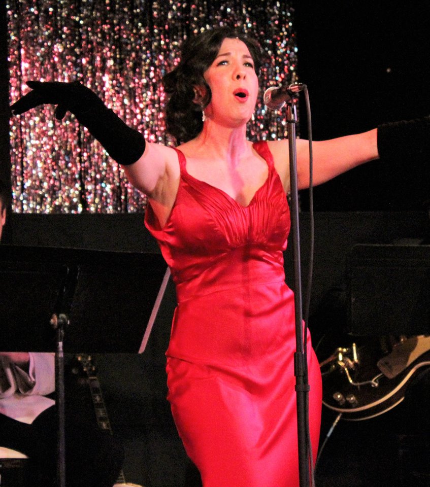 A woman in a red dress passionately singing on stage.