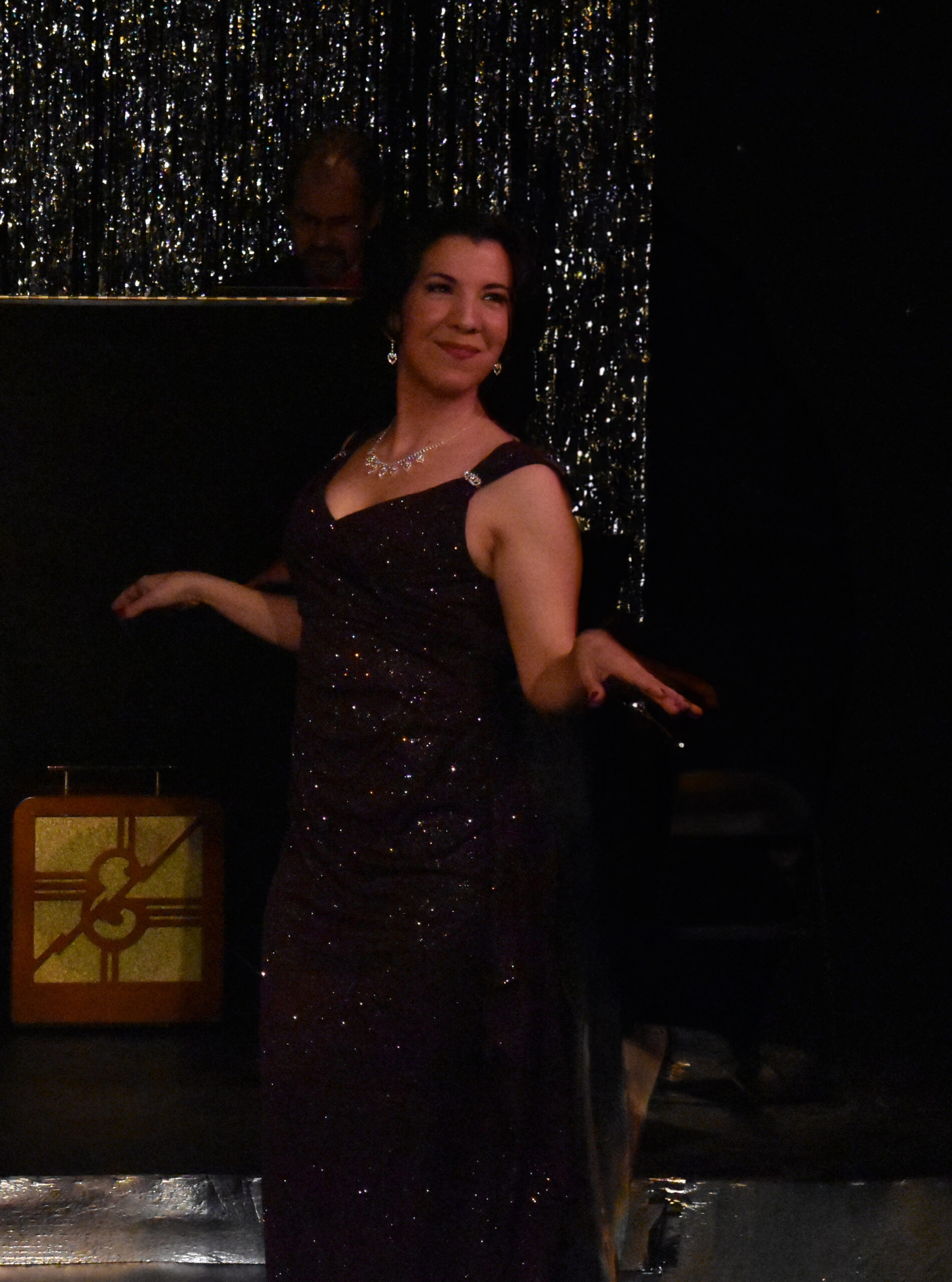 Woman in a dark, sparkly dress posing with arms outstretched.
