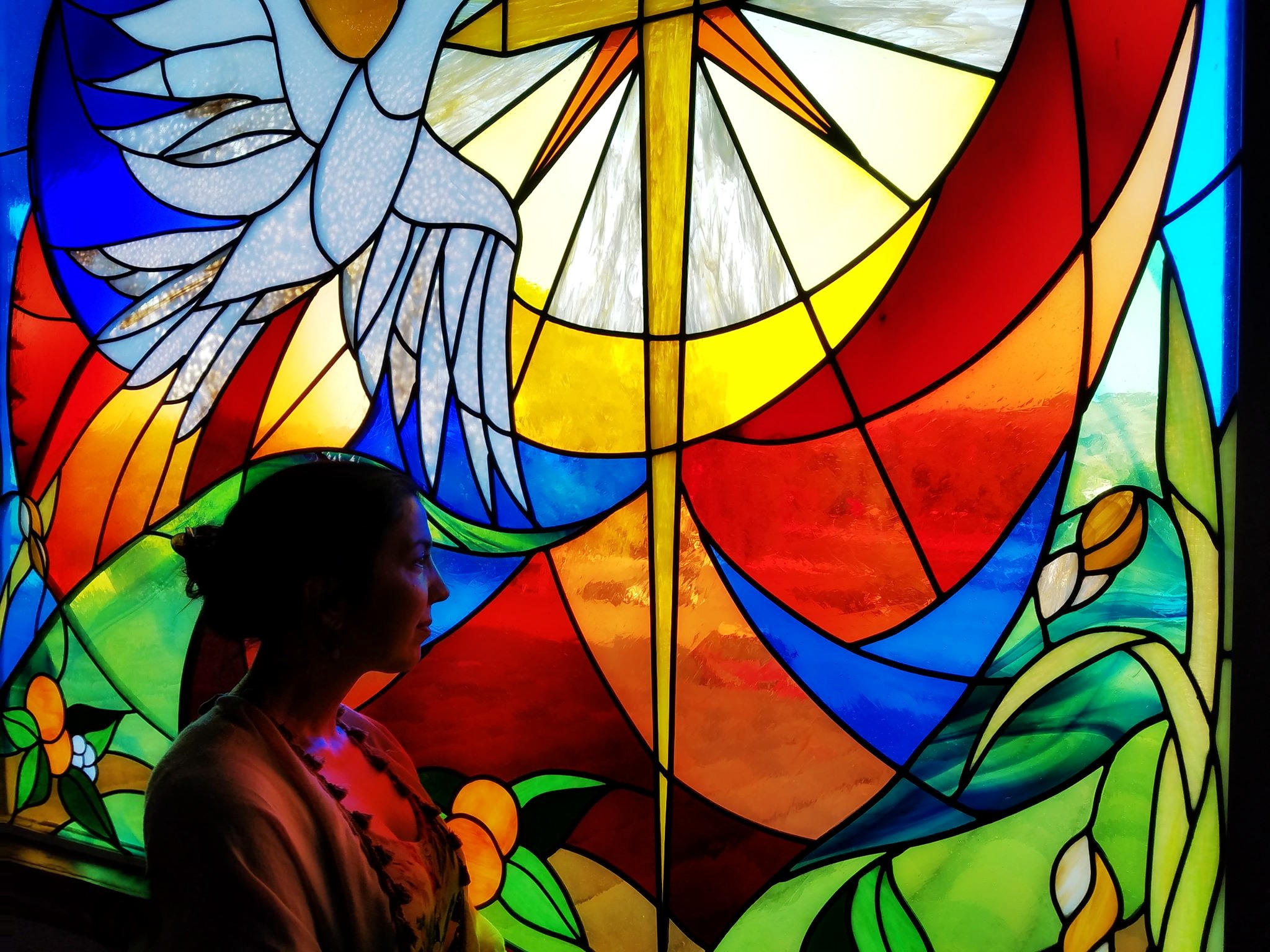 A person admiring a vibrant stained glass artwork featuring a dove and a radiant sun.