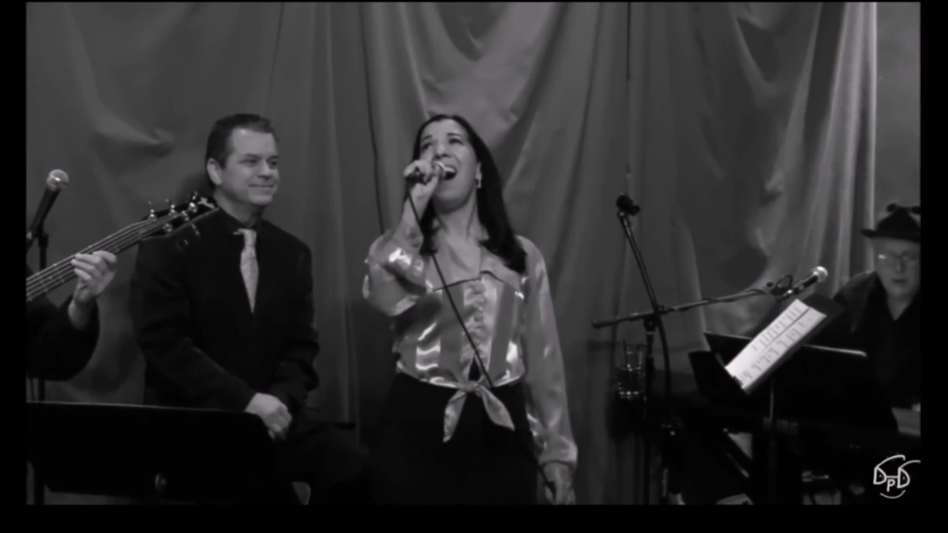 Woman singing on stage with a man seated beside her.