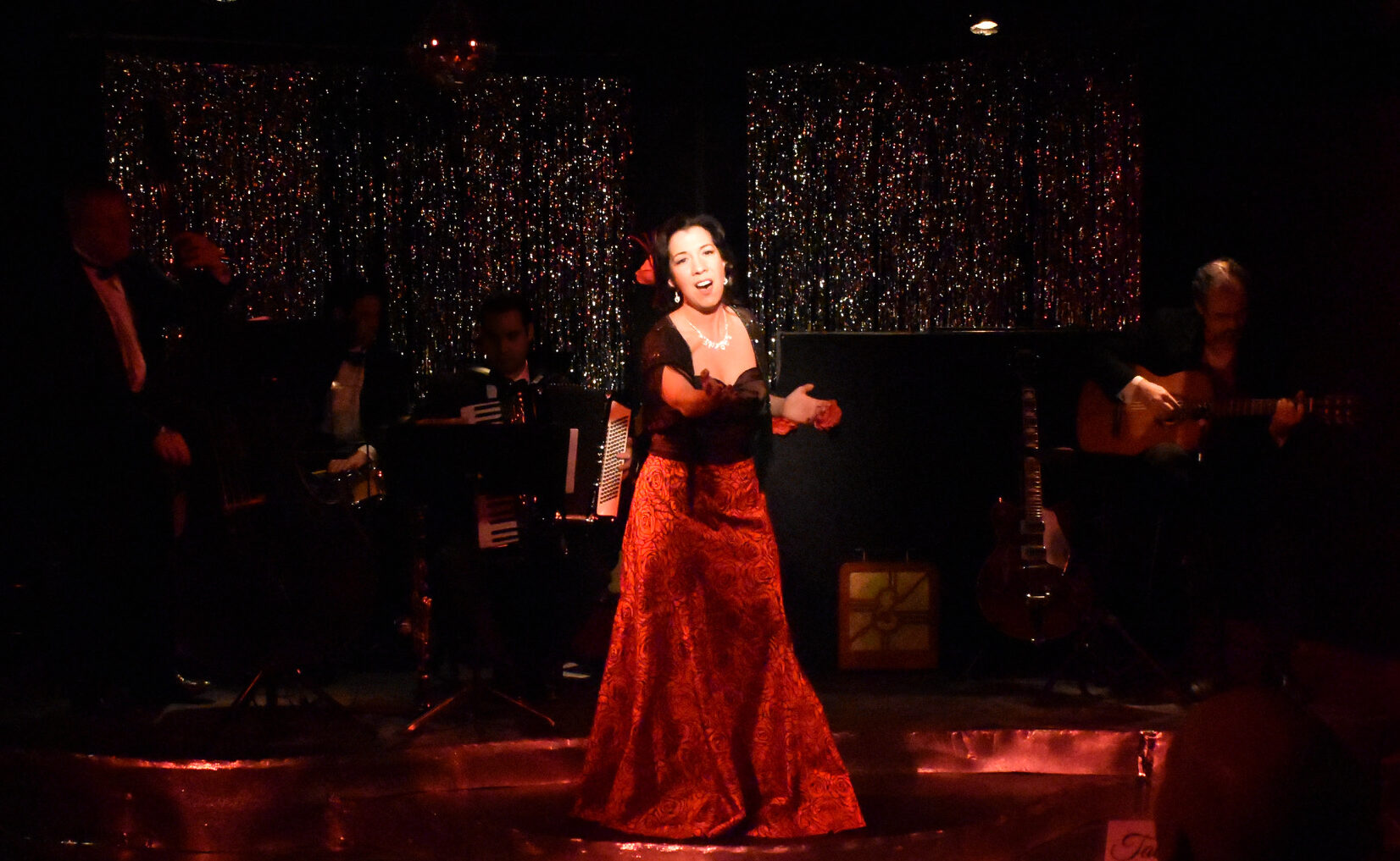 Flamenco dancer in a red dress performing on stage with musicians.