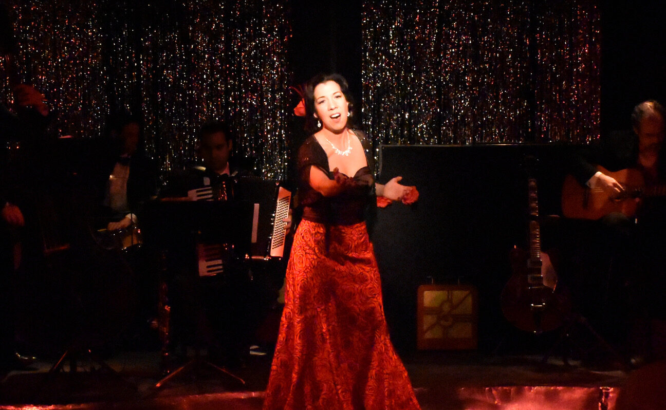 A woman passionately singing on stage in a red dress.
