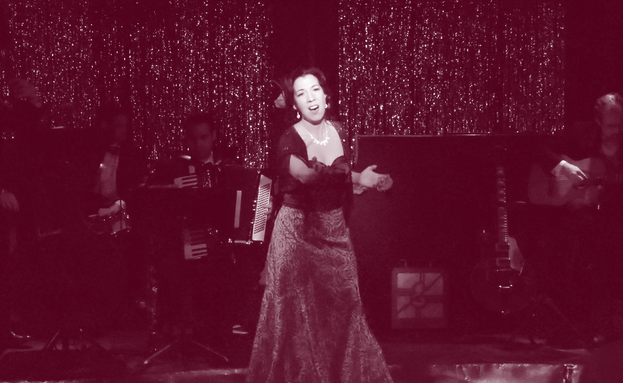 Vintage black-and-white photo of a woman singing on stage in an elegant gown.