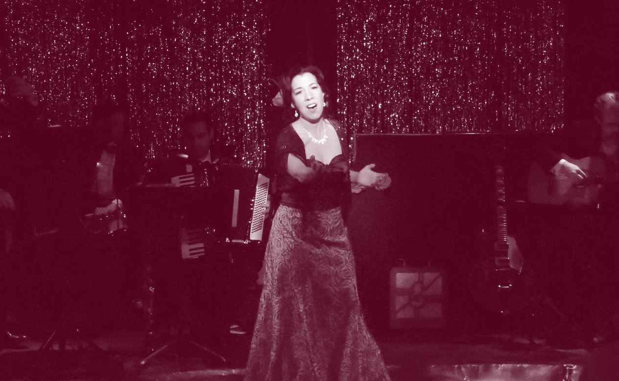 A woman passionately singing on stage in a vintage-style dress.
