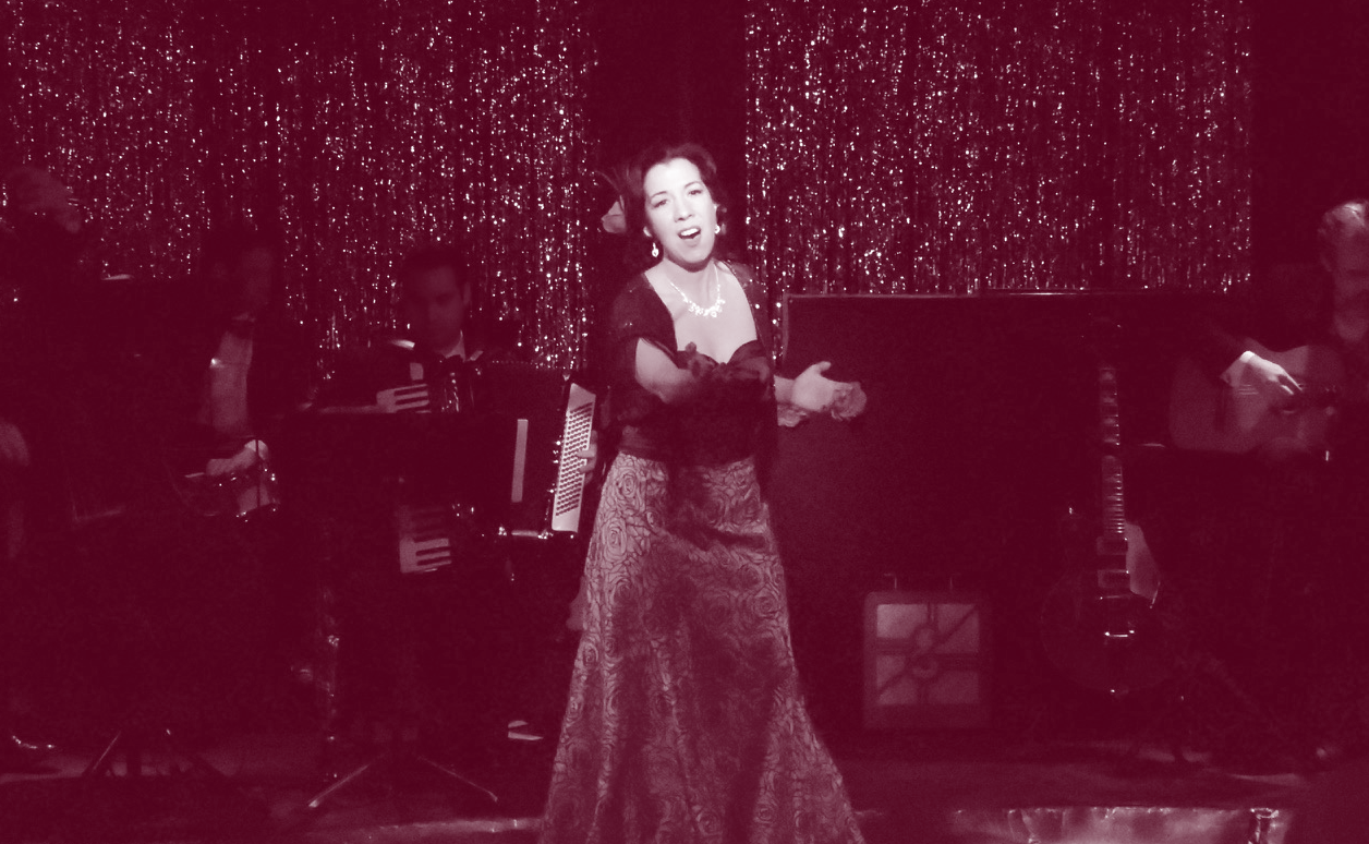 A woman sings passionately on stage in an elegant gown.
