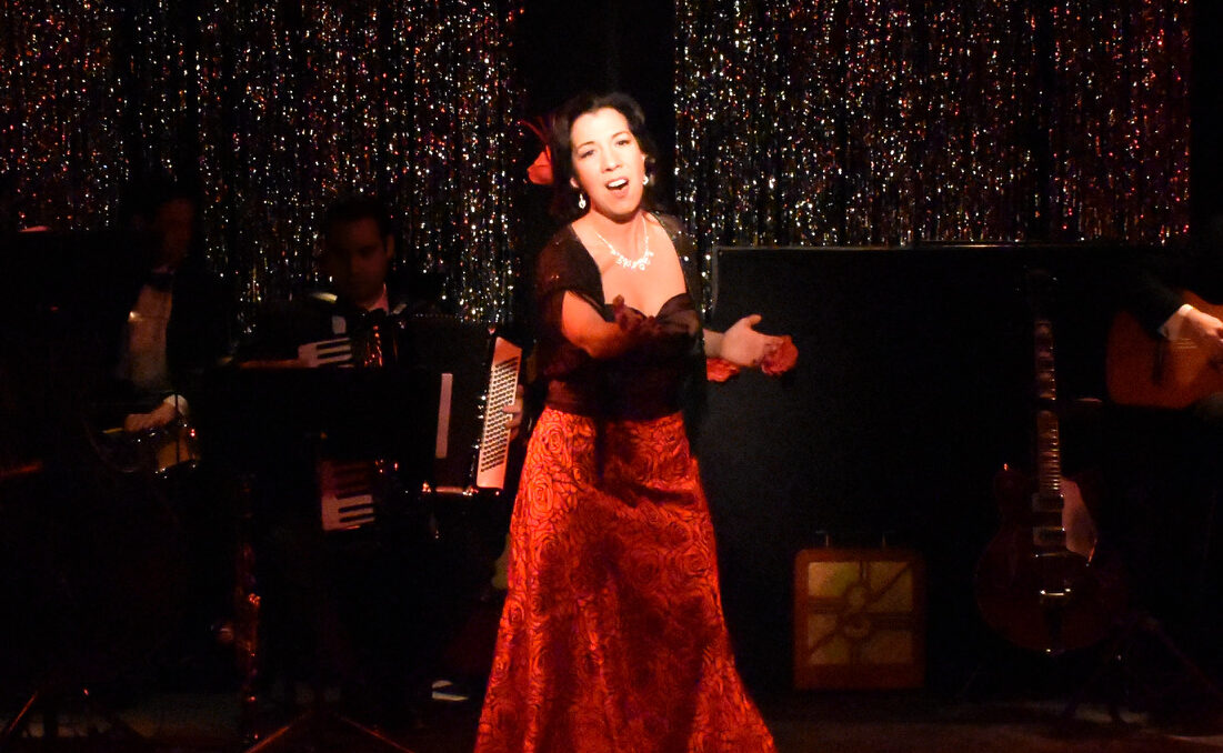 A woman in a red dress passionately singing on stage.