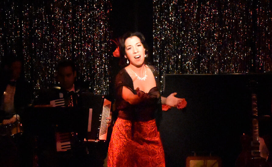 A performer passionately singing on stage in a red dress.
