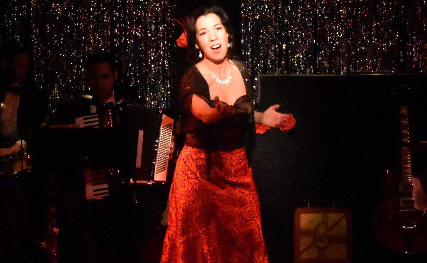 A woman singing passionately on stage in a red dress.