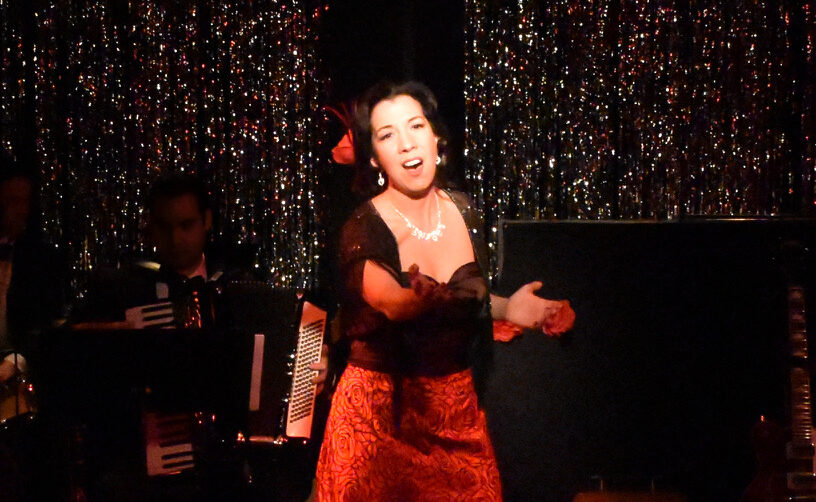A woman passionately singing on stage in a red dress.