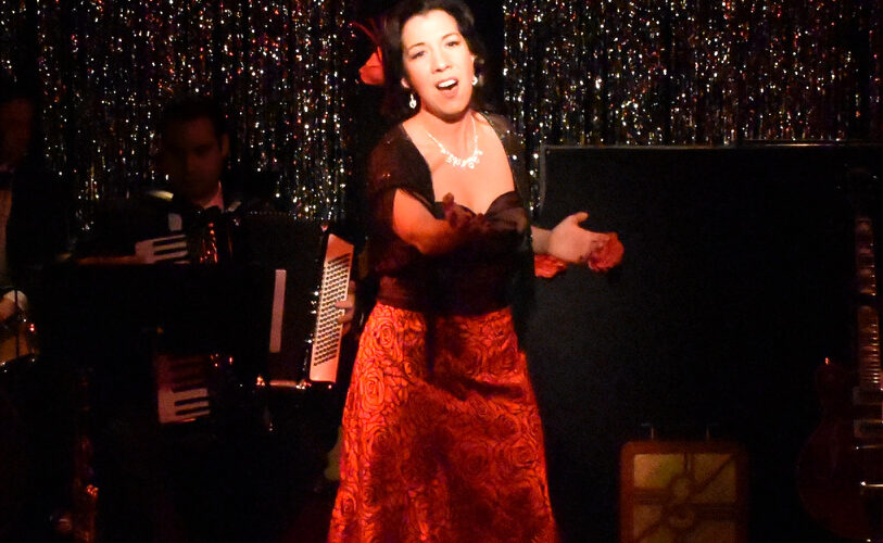 A woman passionately singing on stage in a red dress.