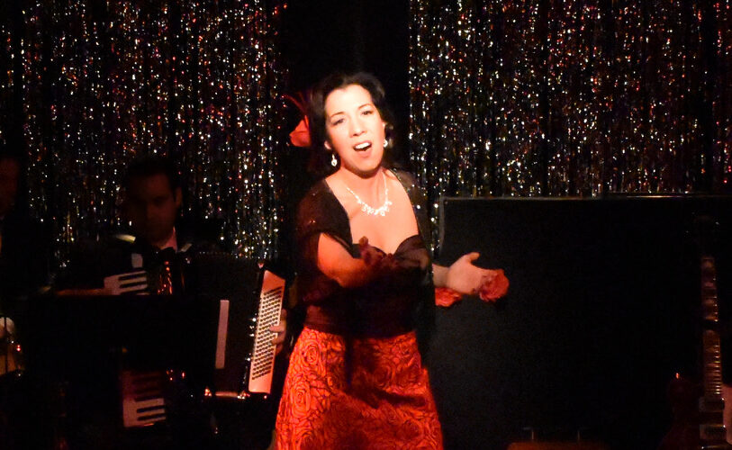 A woman passionately singing on stage with a glittering backdrop.