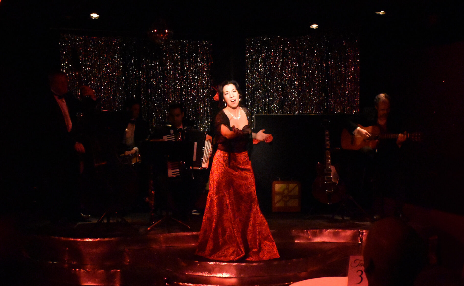 A woman passionately singing on stage in a red dress.