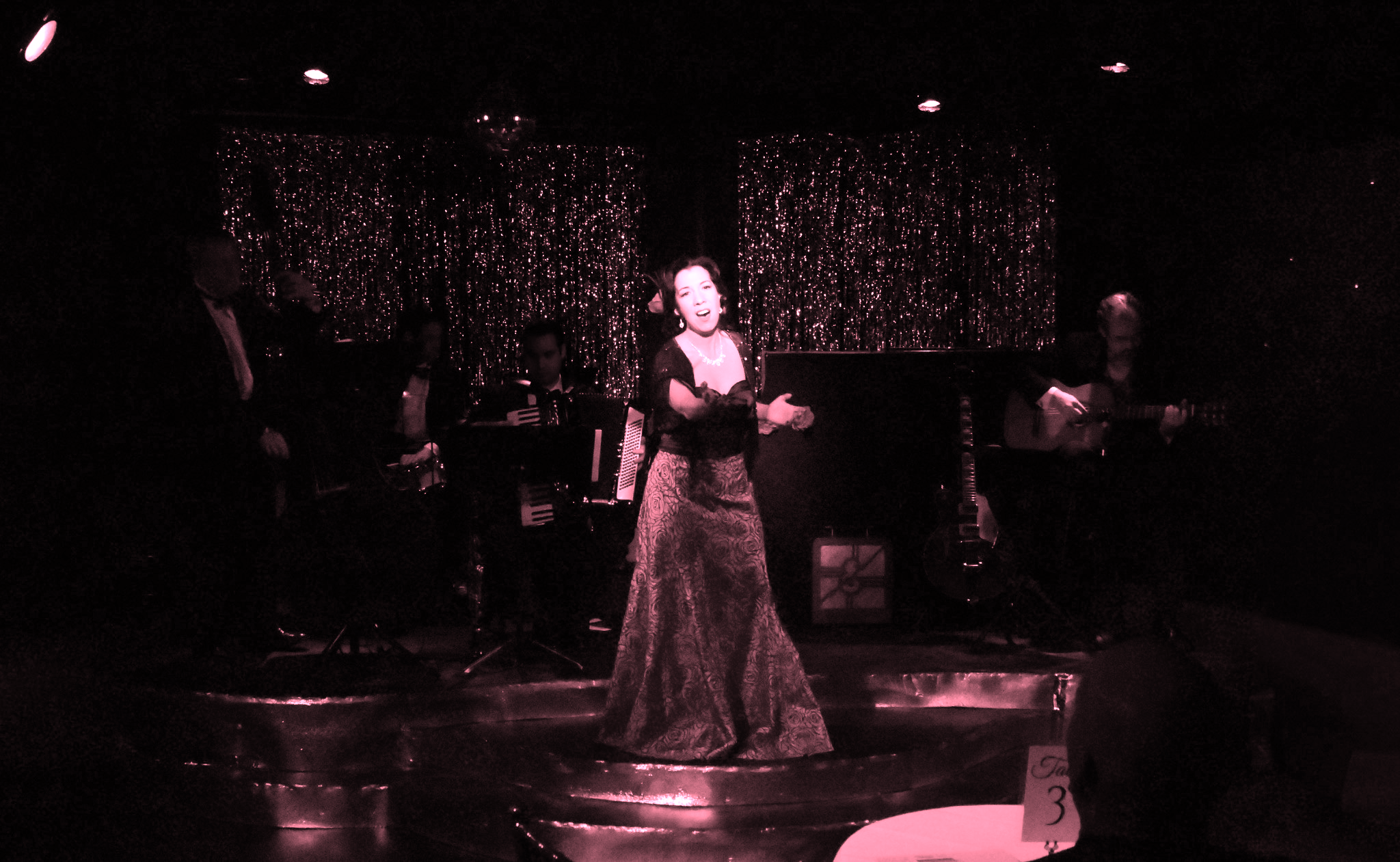 A woman passionately singing on stage in a dimly lit setting.