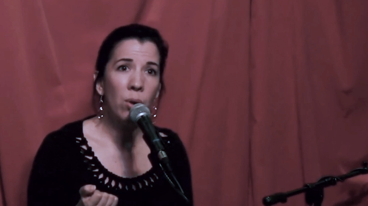 A woman singing into a microphone against a red backdrop.