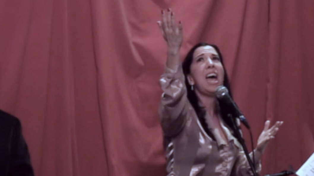 Woman passionately speaking or singing into a microphone with one hand raised.