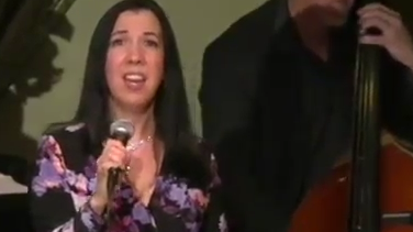 Woman singing into a microphone on stage.